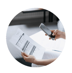 A person holding a cell phone and looking at a piece of paper
