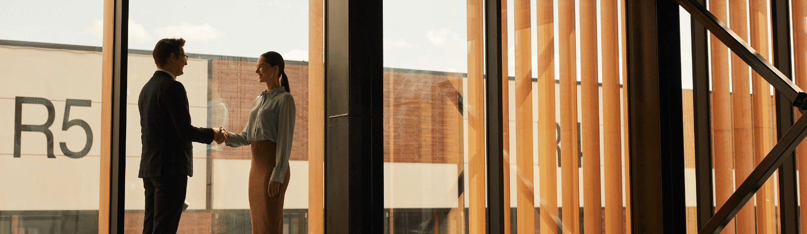 Real estate agent shaking hands with client while standing in empty office building interior lit